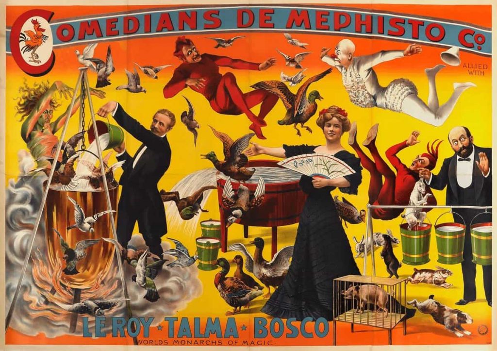 An early 20th century poster for a magic show; in the middle a woman in a black dress holds a fan and gestures with her hand to a man on her right who is pouring water into a cauldron, out of which fly birds. On the left, another man has pulled a rabbit out of a bucket of water. A woman with wild hair stands over the cauldron, while birds and two figures, one dressed as a demon, the other dressed as a clown, fly over the scene. There is a caption: "COMEDIANS DE MEPHISTO CO." written at the top, and at the bottom is written "LEROY, TALMA, BOSCO WORLDS MONARCHS OF MAGIC".