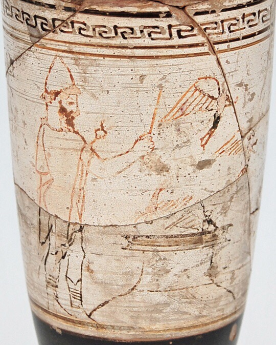 Image of part of a white pottery jug, with a bearded figure on the left in a pointed hat and cloak waving a wand over the opening of a very large jug set into the earth. Two very small winged figures fly out of it, while a third flies in.